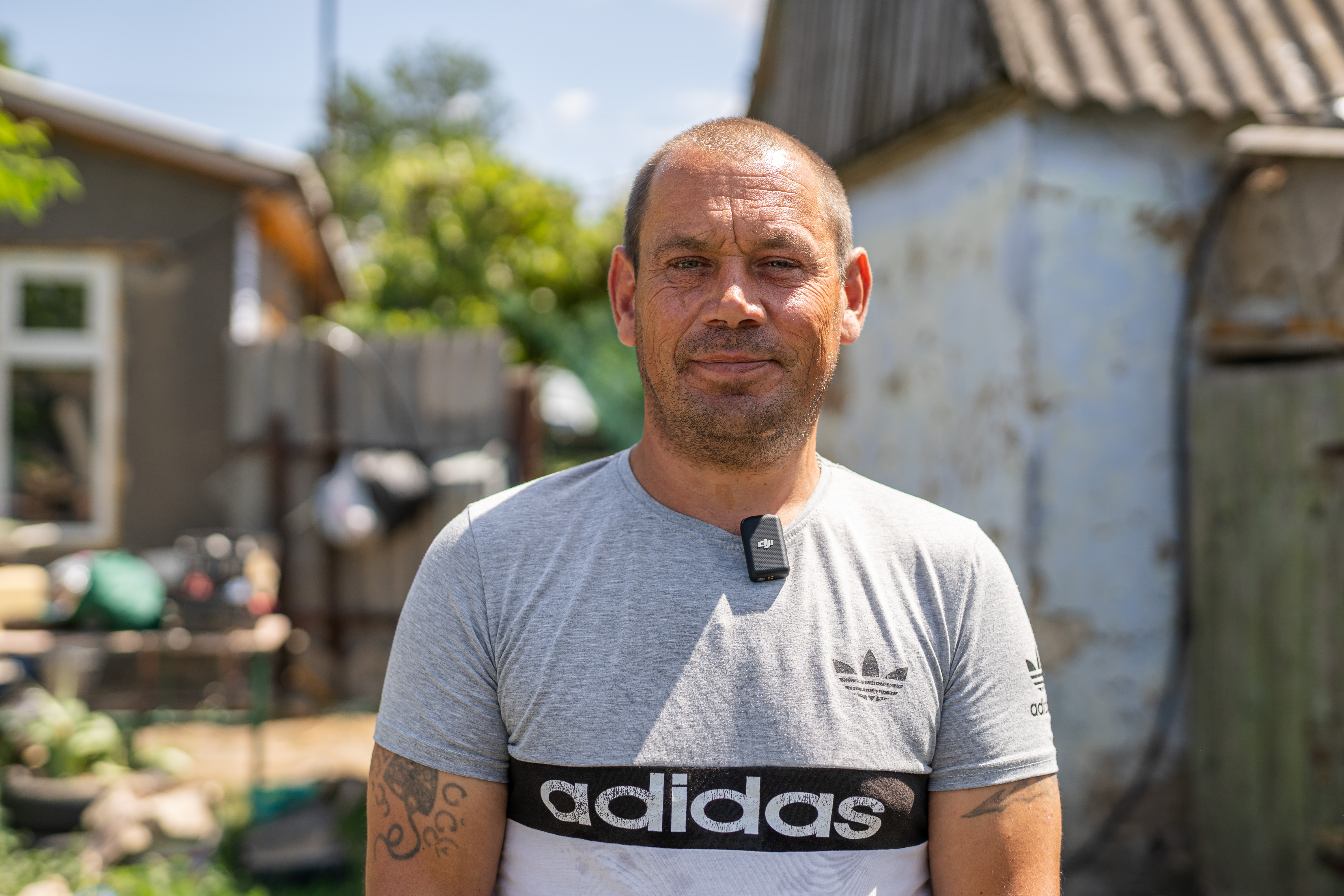 Das Foto zeigt einen Mann mittleren Alters im Portrait. Sein Haar ist kurzrasiert, im Hintergrund ist ein Gebäude in ländlicher Umgebung zu sehen.
