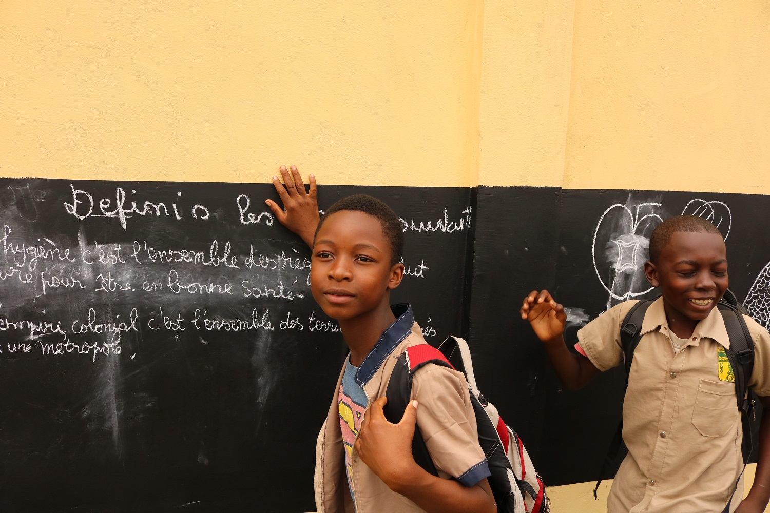 Zwei Schüler stehen vor einer Mauer, an welcher eine Kreidetafel angebracht ist