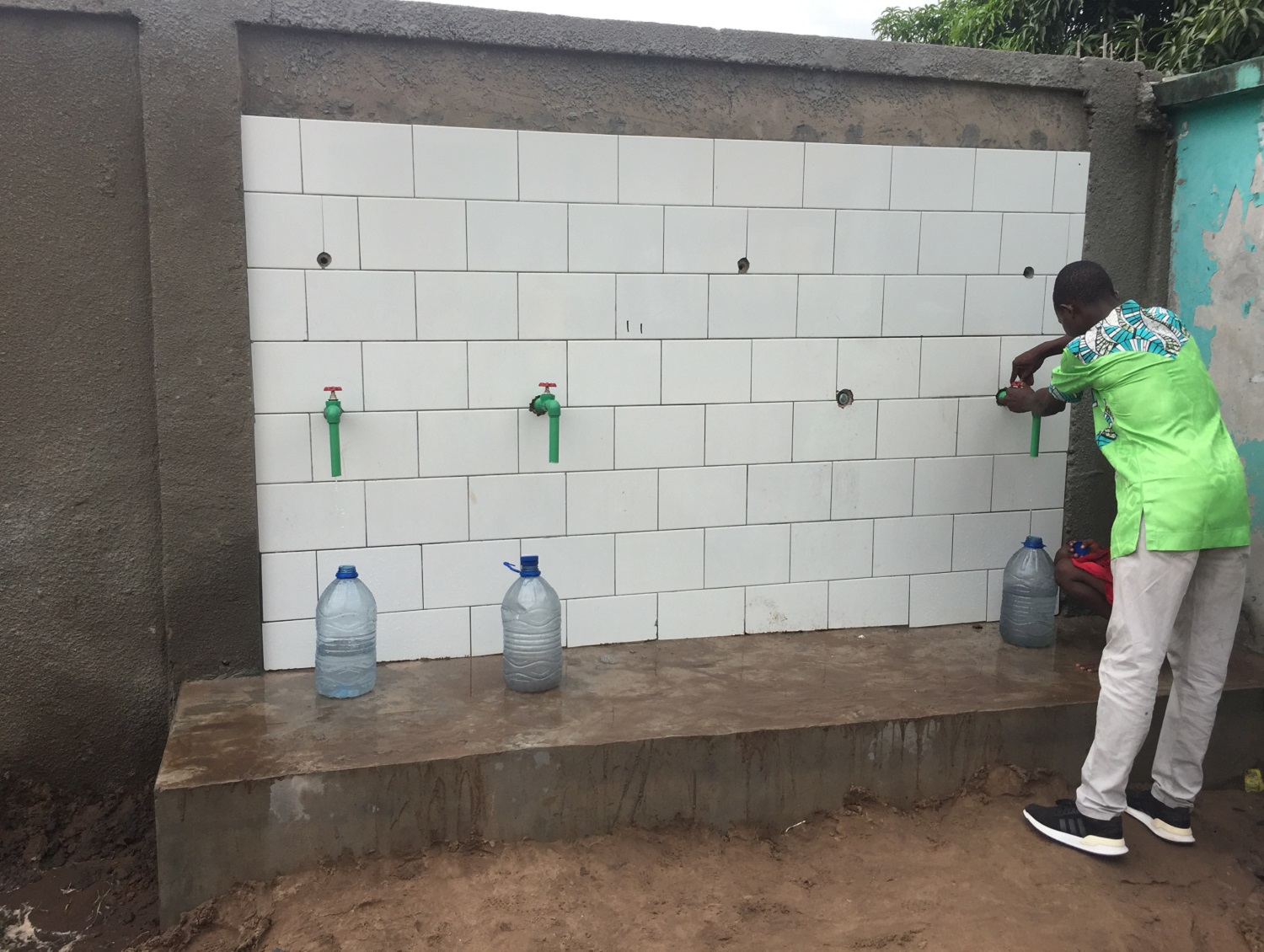 ein Mann steht an einer Wand mit drei Wasserhähnen und füllt Wasser in eine Trinkflasche ab