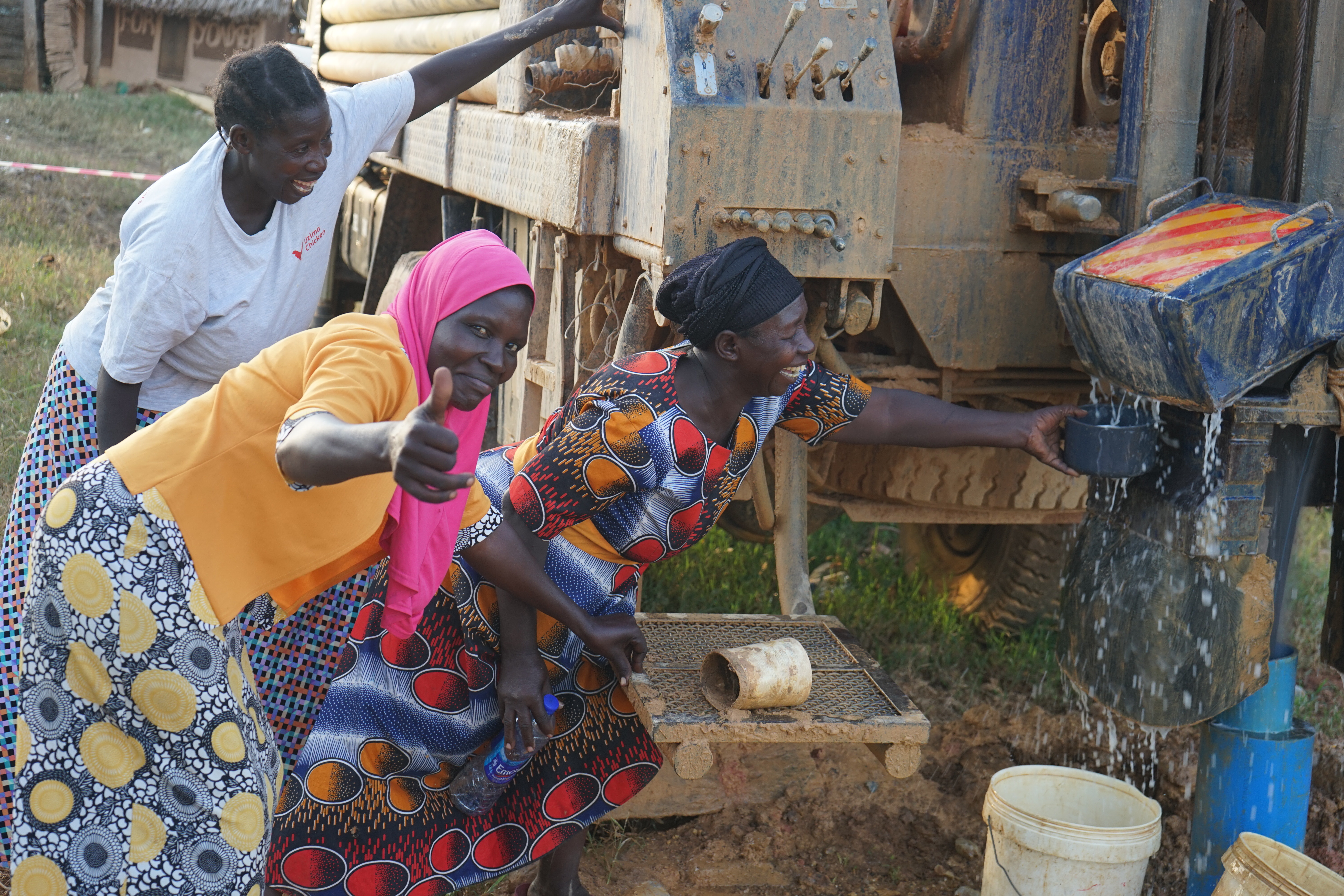 3 Frauen stehen an einem großen, mit Technik ausgestatteten Fahrzeug, neben einem großen Rohr fließt Wasser