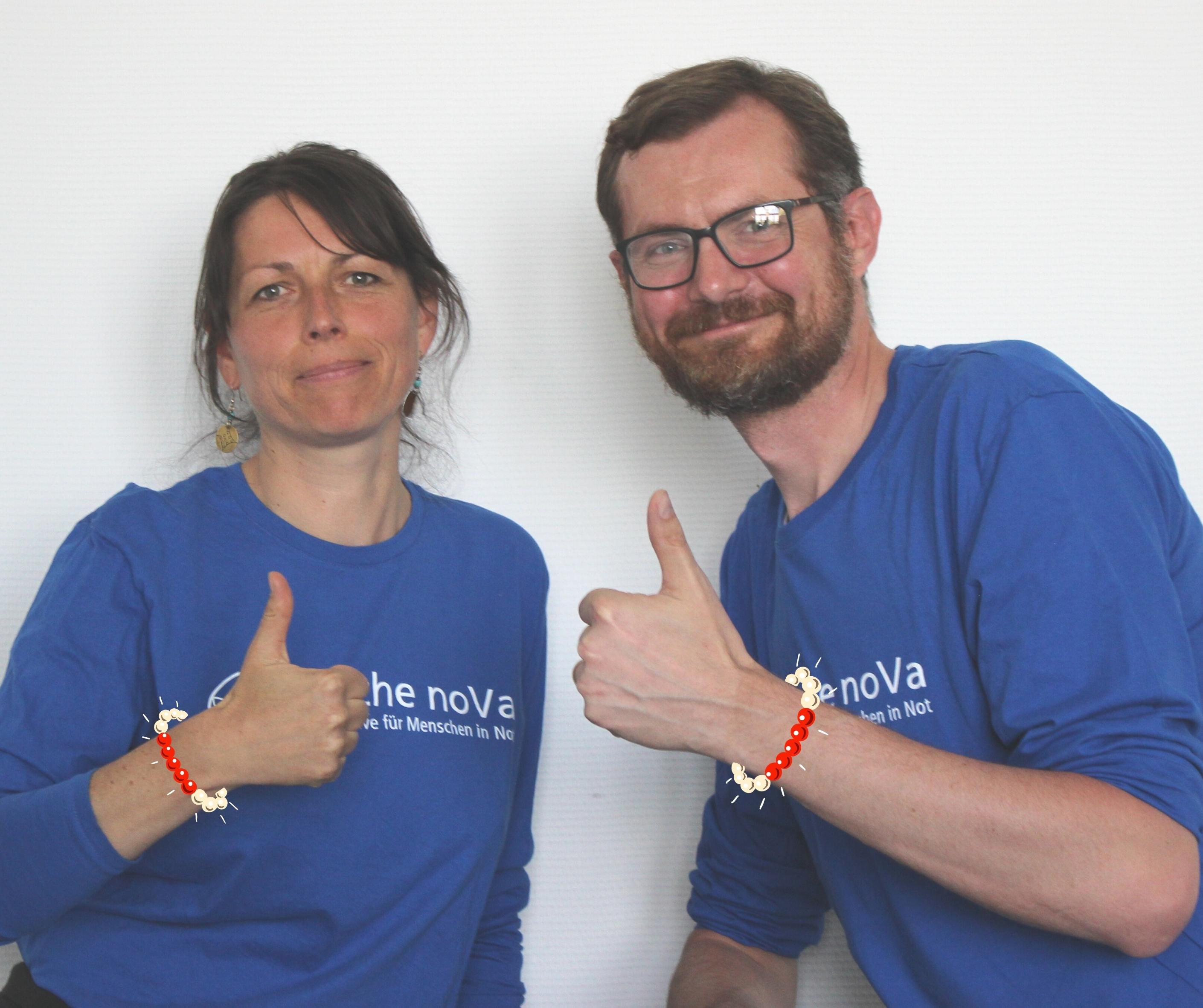 Yvonne Stephan (links) und Mathias Anderson (rechts) schauen in die Kamera mit Daumen hoch, am Arm ein Armband als grafisches Symbol für Menstruationshygiene