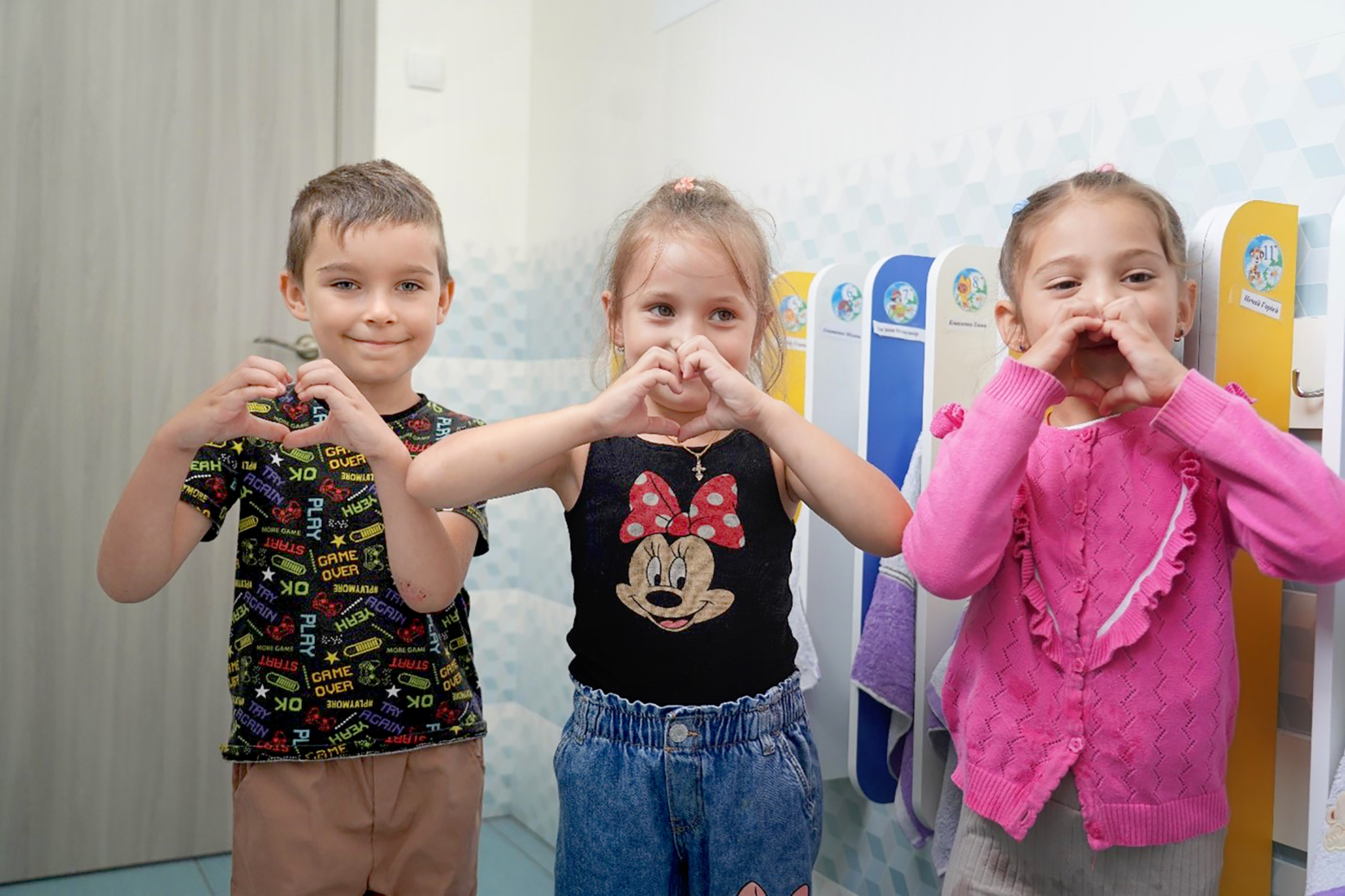 Drei Kinder im Vorschulalter stehen nebeneinander und formen mit ihren Händen ein Herz.