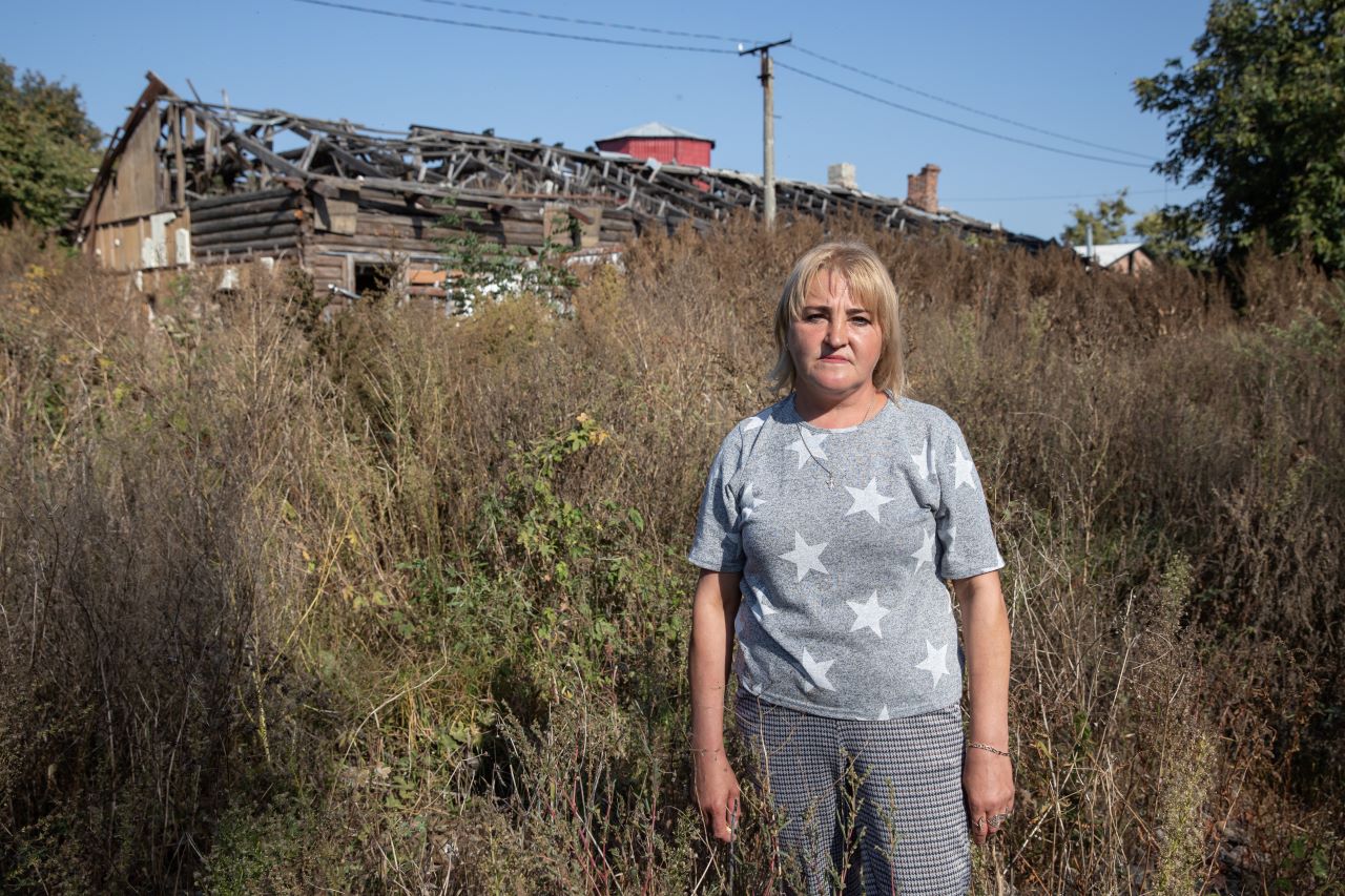 The picture shows social worker Liudmyla Brovko standing in front of the ruins of her former home.