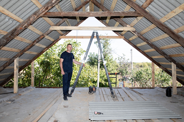 Volodymyr Novytska stands in front of a ladder under the roof of his house, which he is currently repairing.
