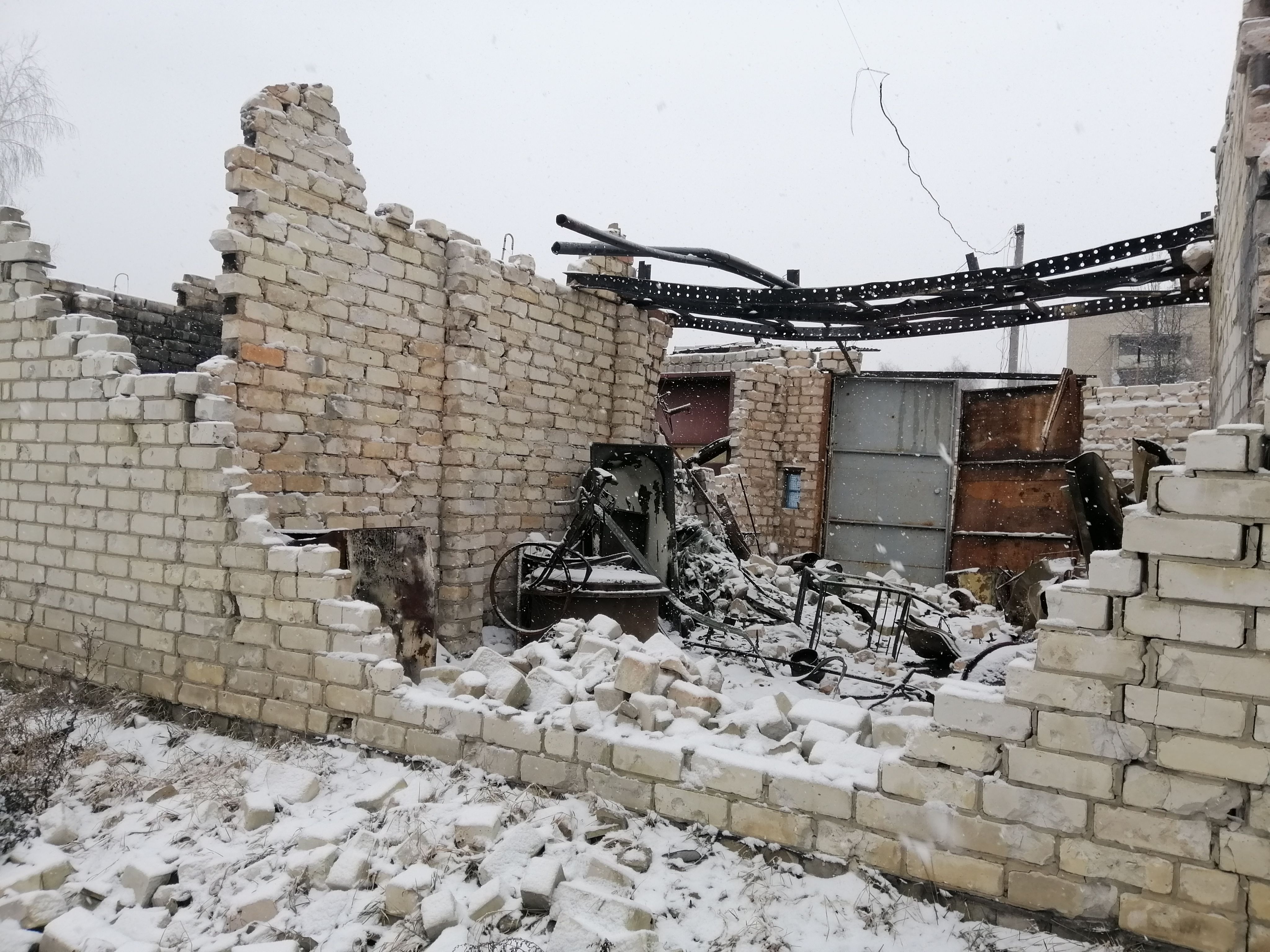 Das Bild zeigt ein Gebäude, das bis auf das Mauerwerk zerstört wurde. Auf der Ruine des Hauses liegt Schnee.