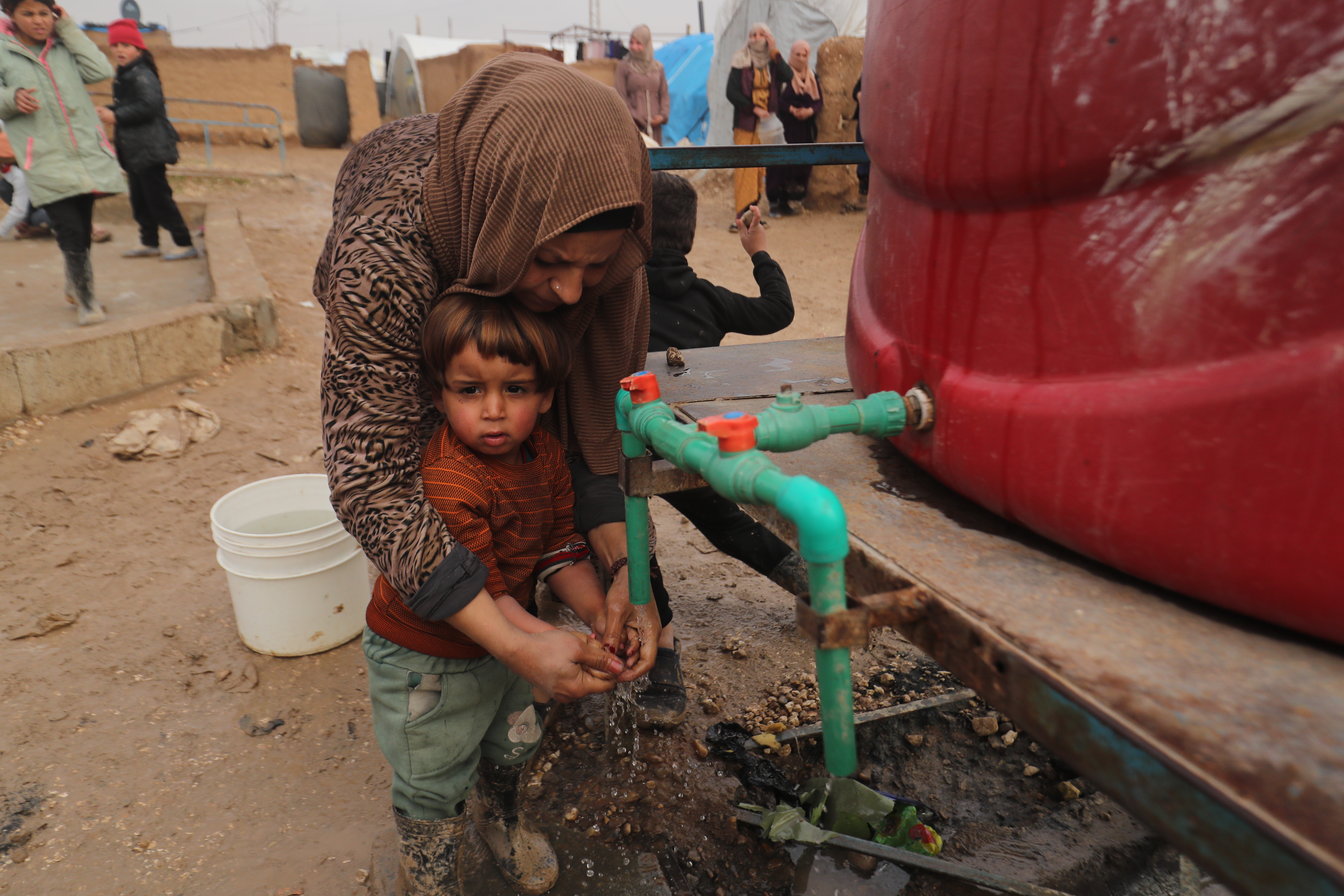 Frau und Kind stehen am Wasserhahn eines Wassertanks, die Frau hilft dem Kind beim Händewaschen