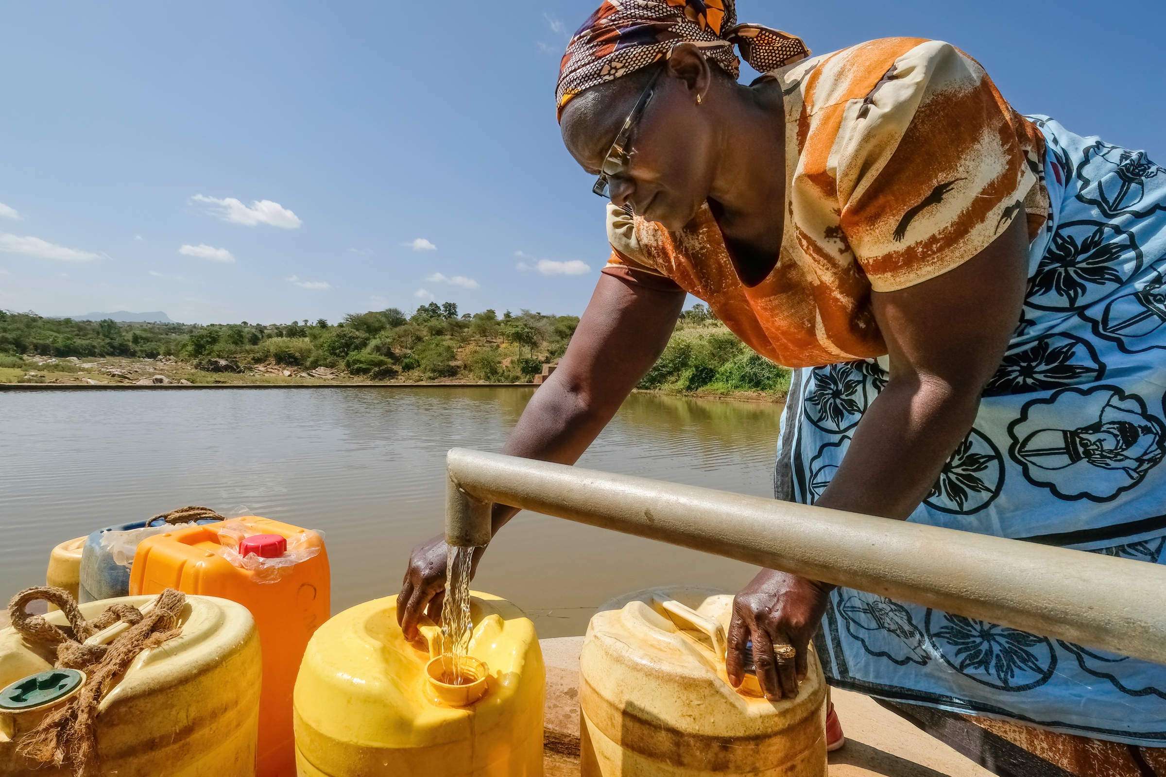 Frau füllt Wasserkanister an Sanddamm mit Wasser