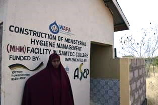 Nimo, eine Frau mit Umhang, steht vor einer Toilette