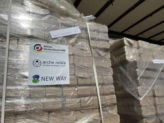 Ein verpackter Stapel Holzbriketts beschriftet mit den Logos von ADH, arche noVa und New Way steht in einem LKW zur Verteilung bereit