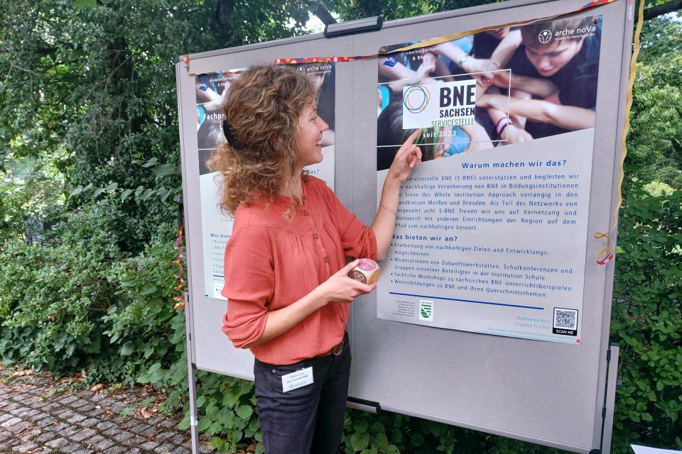 Frau steht an einer Informationstafel zum Thema BNE und zeigt mit dem Finger darauf