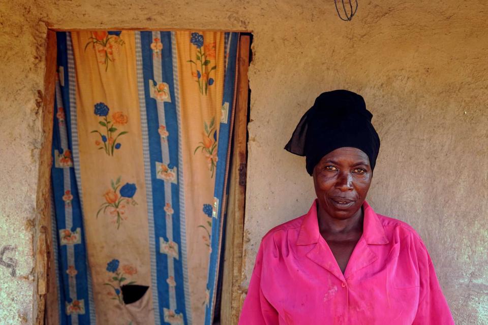 Portrait einer Frau vor einer Hauswand, neben ihr ein Durchgang, der mit einem Stück Stoff verhangen ist.